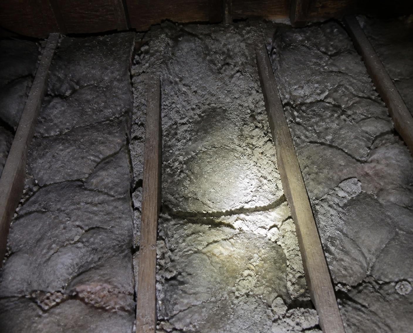 Old, compressed attic insulation lying unevenly between the joists