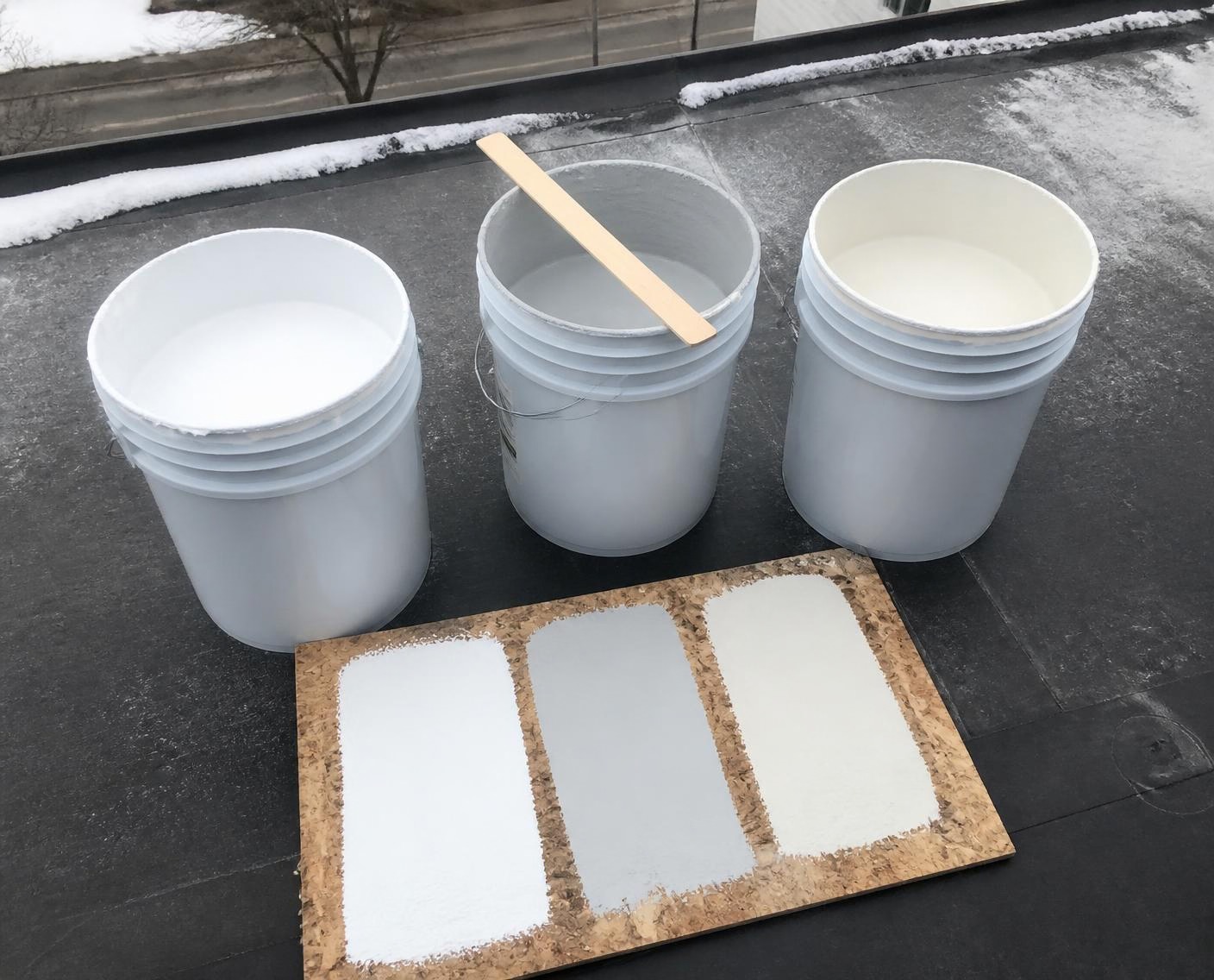 Open pails of different roof coating types on a roof