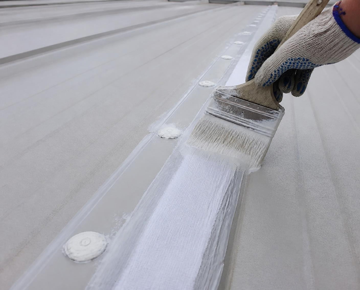 Reinforcing fabric bedded into sealant over a roof seam before coating