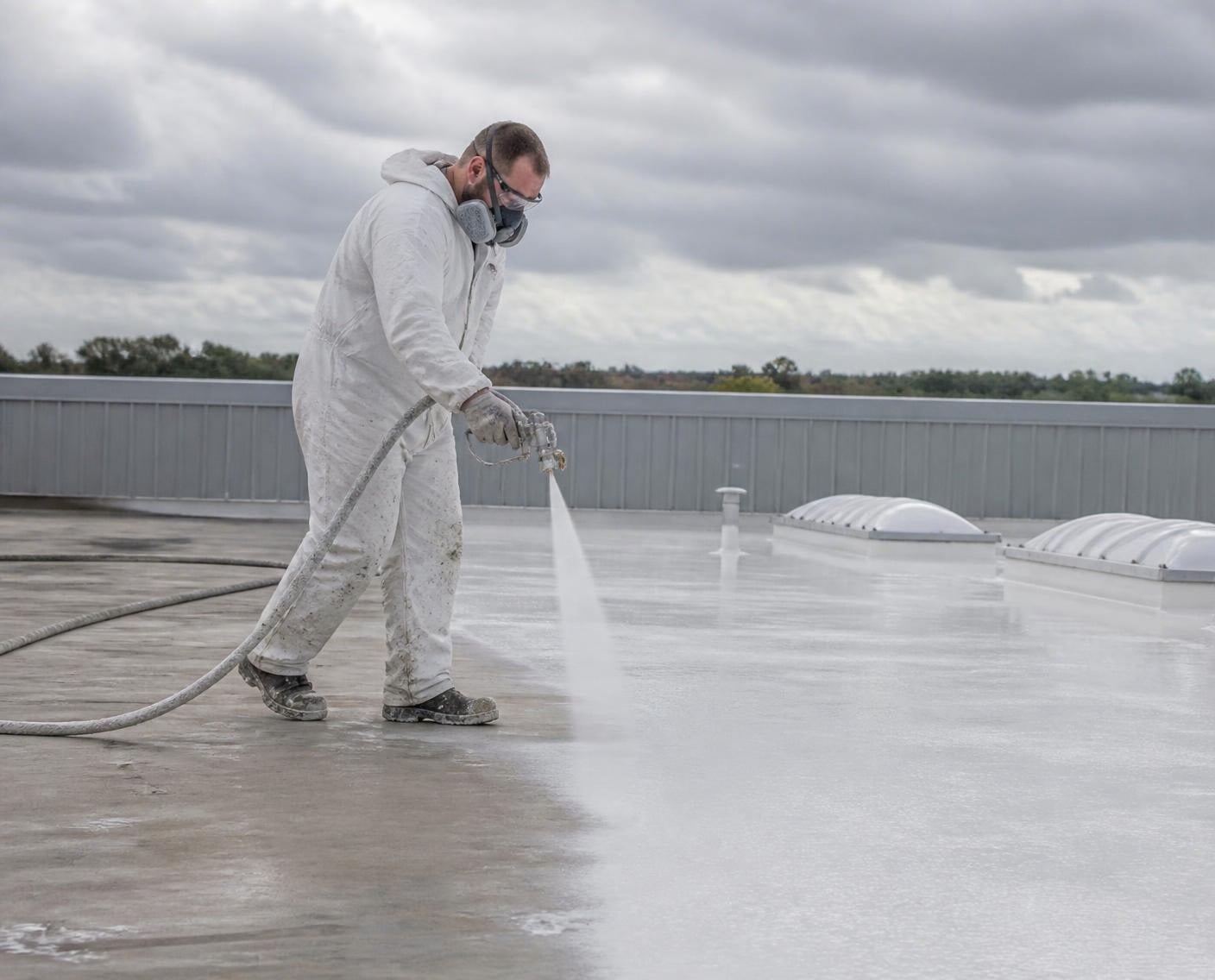 Silicone roof coating being sprayed across a flat commercial roof